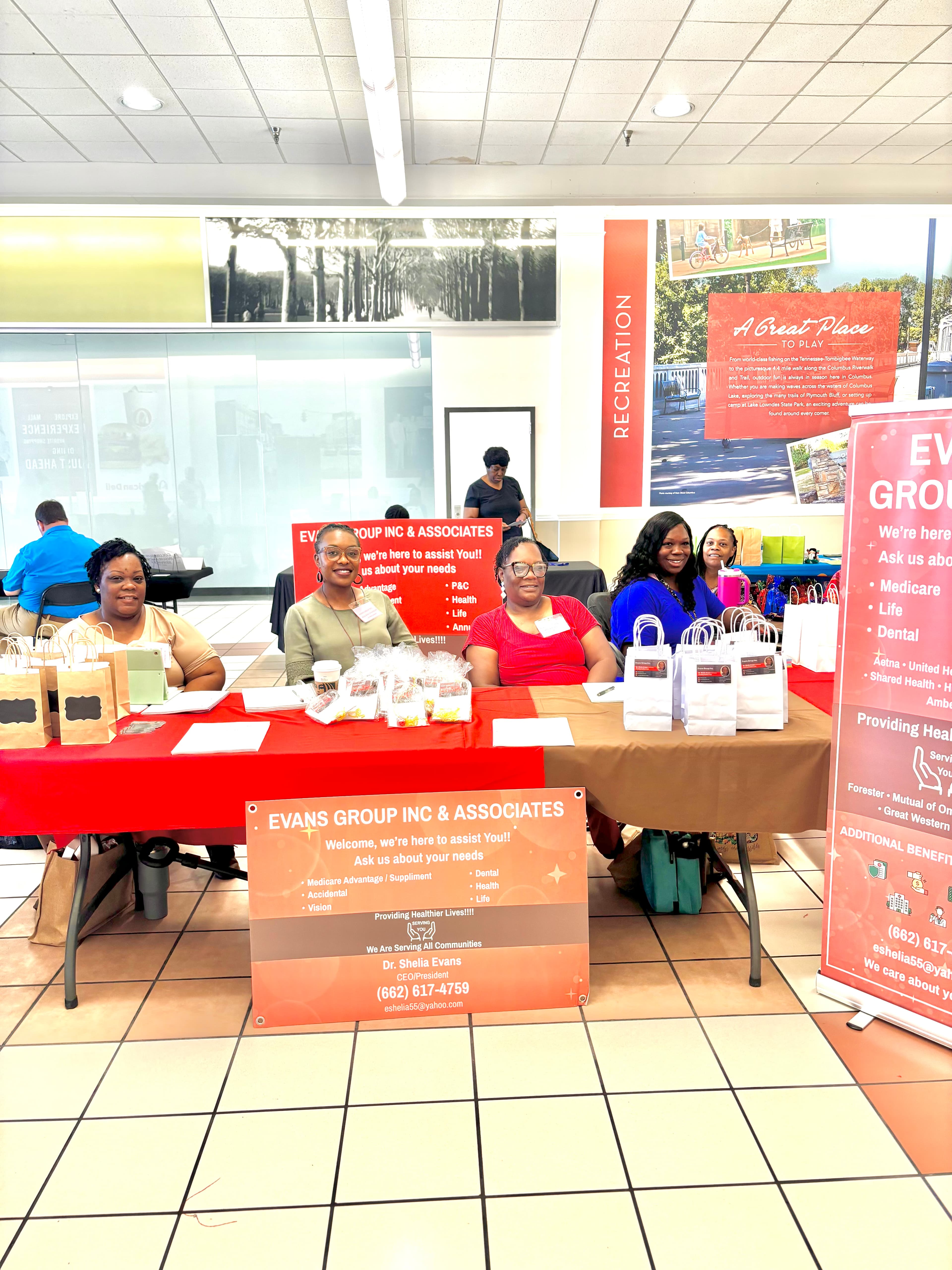 Five women at an Evans Group Inc & Associates promotional table with gift bags.
